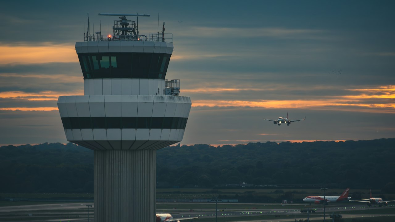 An airport control tower and apron lights at dusk, the sky shifting from orange to deep blue